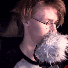 a close up of a person wearing glasses and holding a furry object in their mouth