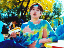 a man wearing a tie dye sweater is eating a hot dog