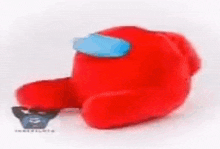 a red among us stuffed animal with a blue mask on its face is sitting on a white surface .