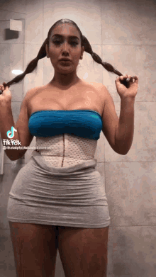 a woman wearing a blue top and a grey skirt has a tiktok sticker on her shoulder