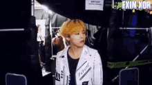 a young man with yellow hair is standing in front of a sign that says artist quick orange
