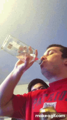 a man in a red patriots shirt drinks from a glass bottle