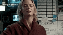 a woman in a red robe is standing in front of a wall with a calendar on it .