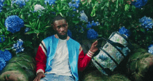 a man in a blue jacket sits on a couch holding a bag