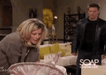 a man and a woman are standing in a living room . the man is wearing a black leather jacket .