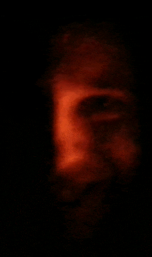 a blurry picture of a man 's face in the dark with a red light coming out of his eyes .