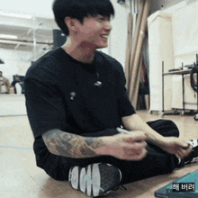 a man with a tattoo on his arm is sitting on the floor and smiling