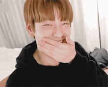 a young man is covering his mouth with his hands and smiling