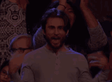 a man with a beard is sitting in a crowd of people and applauding .
