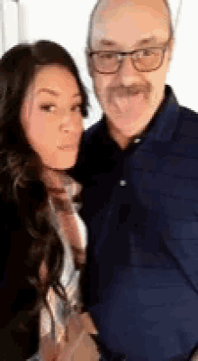 a man with glasses and a mustache is standing next to a woman with her tongue out .