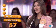 a woman in a pink jacket stands in front of a screen that says m-n- jamon and 57