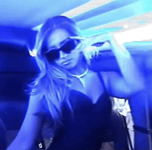 a woman wearing sunglasses and a necklace is dancing in a blue room
