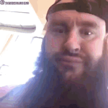 a man with a beard is wearing a hat and looking at the camera .