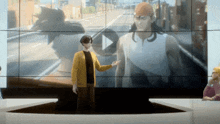 a man in a yellow sweater is standing in front of a large screen with a man in a white tank top on it