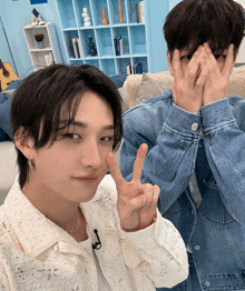 two young men covering their faces with their hands in front of a blue bookshelf