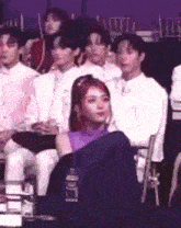 a woman in a purple top is sitting in a chair in front of a crowd of people .