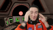 a man wearing headphones and a nasa jacket adjusts his ears