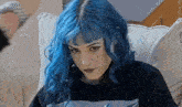 a girl with blue hair and a nose ring is sitting on a couch .