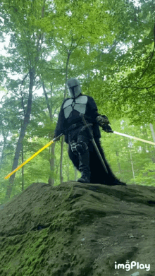 a man in a knight 's costume is holding a yellow lightsaber in the woods