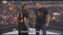 two men in a wrestling ring one of whom is wearing a shirt that says shake my hand