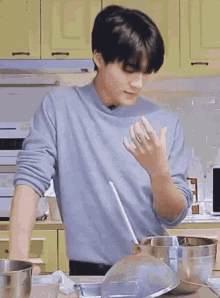 a young man is standing in a kitchen preparing food with a spoon .