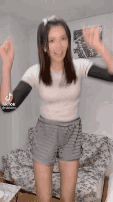 a woman in shorts and a white shirt is dancing in a living room with her hands in the air .