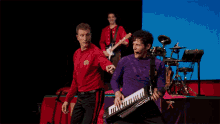 a man in a purple shirt is holding a keyboard while another man in a red shirt is playing a guitar