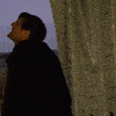 a man in a black jacket is standing in front of a window and making a funny face