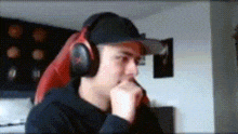 a man wearing headphones and a hat is sitting in a chair with his hand on his chin .
