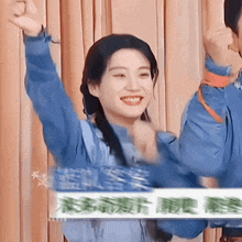 a woman in a blue shirt is smiling and raising her arms in the air
