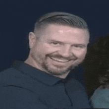 a man with a beard is smiling for the camera in a blue shirt .