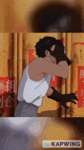 a man in a white tank top and black gloves is standing in front of a yellow wall with chinese characters on it