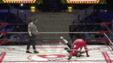 a referee is standing in the middle of a wrestling ring watching two wrestlers wrestling .
