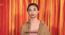 a woman wearing a mayward shirt is standing in front of a colorful background