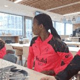 a woman wearing a pink and black asahi shirt sits at a table