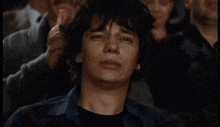 a man sitting in a crowd with his eyes closed and his hand on his head
