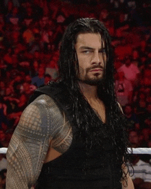a man with long hair and a beard is standing in front of a crowd in a wrestling ring .