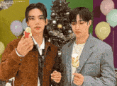 two men are standing next to each other in front of a christmas tree holding marshmallows on sticks .