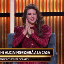 a woman in a red dress is sitting in a chair with her hands folded in front of a sign that says the alicia