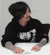 a man with tattoos on his arms is wearing a black hoodie with a picture of a woman on the front