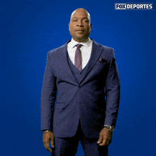a man in a suit and tie stands in front of a blue background that says fox deportes on it