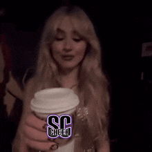 a woman with long blonde hair is holding a cup with the letter s on it