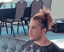 a man with a ponytail is sitting on a couch in front of chairs