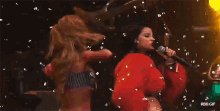 two women singing into microphones with confetti falling in the background
