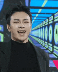 a man in a black suit and turtleneck is smiling in front of a row of numbers .