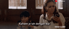 a woman holding a cell phone next to another woman with the caption " kawin je lah dengan dia "