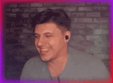 a man wearing earbuds smiles in front of a brick wall