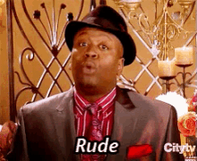 a man in a suit and hat says rude in front of candles