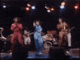 a man in a blue jumpsuit is singing into a microphone