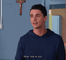 a man in a blue hoodie is standing in front of a cross and talking to another man .
